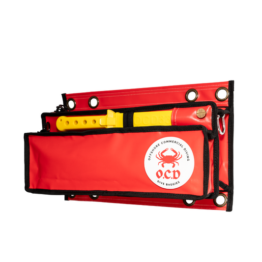 A red OCD Dive Baggie with a dual-pocket design, featuring a yellow tool in the upper pocket and black mesh pouches. The bag has brass eyelets, a logo, and is displayed against a white background.